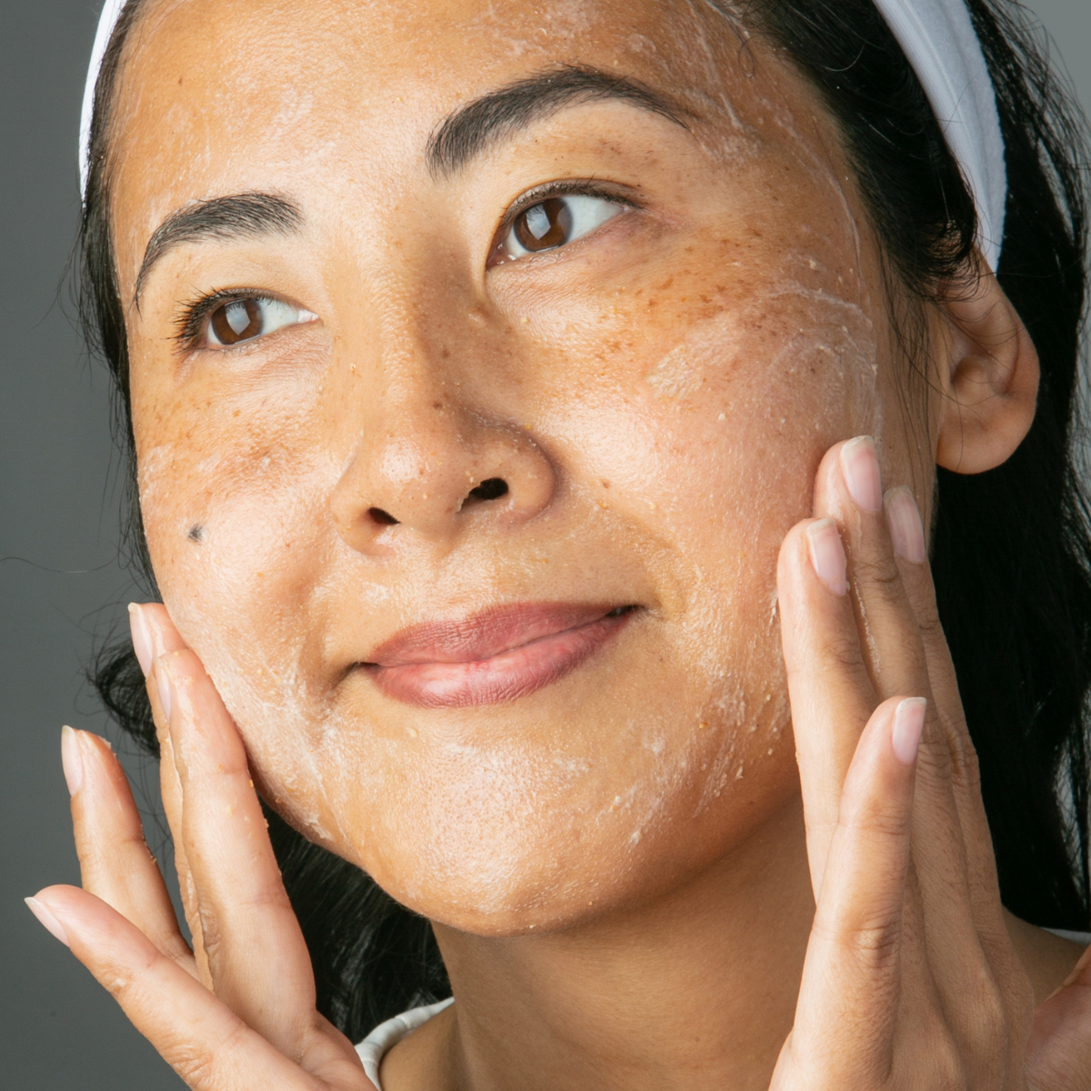 TOO MUCH OF A GOOD THING: WHAT TO DO IF YOU’VE OVER-EXFOLIATED: a woman applying scrub to her cheeks and smiling