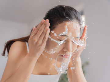 an asian woman splashing her face with water