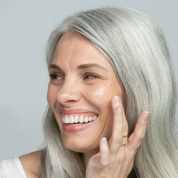 8 WAYS TO INCREASE SKIN’S COLLAGEN AND FIRMNESS: an image of a pretty, mature woman putting some skincare product on her cheek and smiling