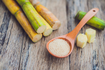 An image of sugar cane stalks and crystals in a spoon on wooden background