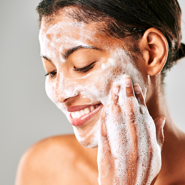 a medium-skinned woman sudsing up foam on her cheek and smiling