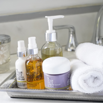 Easy Steps to a Basic Skincare Routine! A group of IN YOUR FACE SKINCARE products on a tray in a bathroom with a faucet behind them and towels beside them