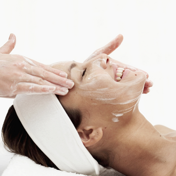 a woman smiling, getting a facial on a white background