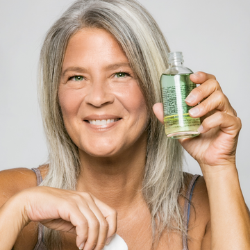 SKINCARE MYTHS: TO TONE, OR NOT TO TONE: a smiling, mature woman is holding up a bottle of IN YOUR FACE CITRUS CUCUMBER TONER