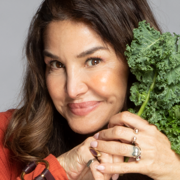 a woman holding kale next to her face, smiling