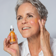 grey-haired woman holding a bottle of the BAKUCHIOL WONDER SERUM