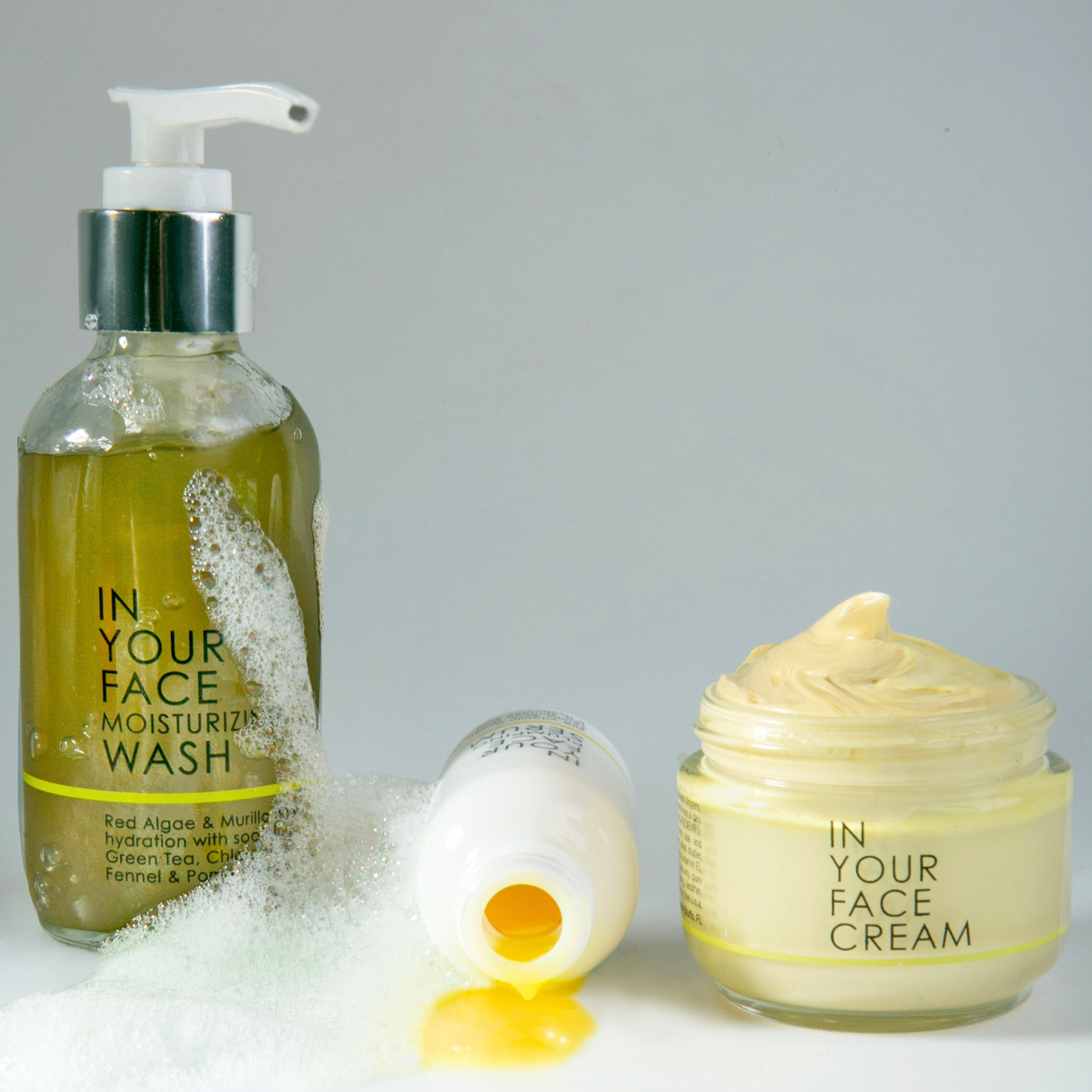 an image of the 3 STEP ESSENTIALS on a white background. The PLUMPING SERUM is tipped over, showing the yellow-ish texture. Foam bubbles surround the bottles.