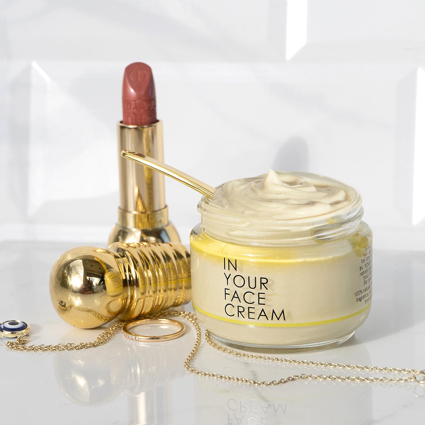 lifestyle shot of IN YOUR FACE CREAM next to lipstick and jewelry