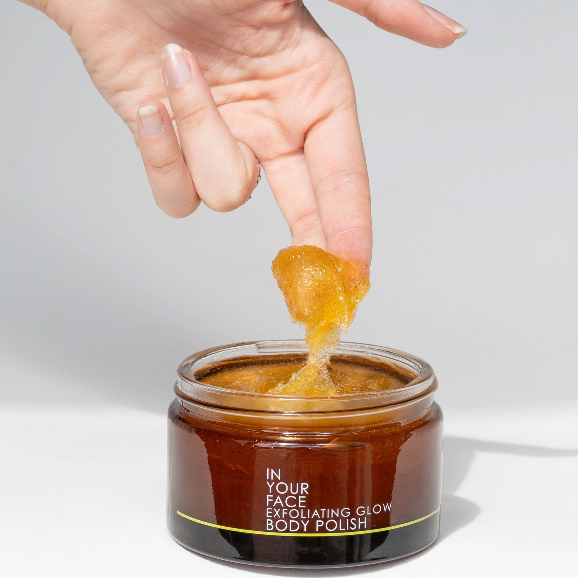 jar of exfoliating glow body polish with fingers dipping into it