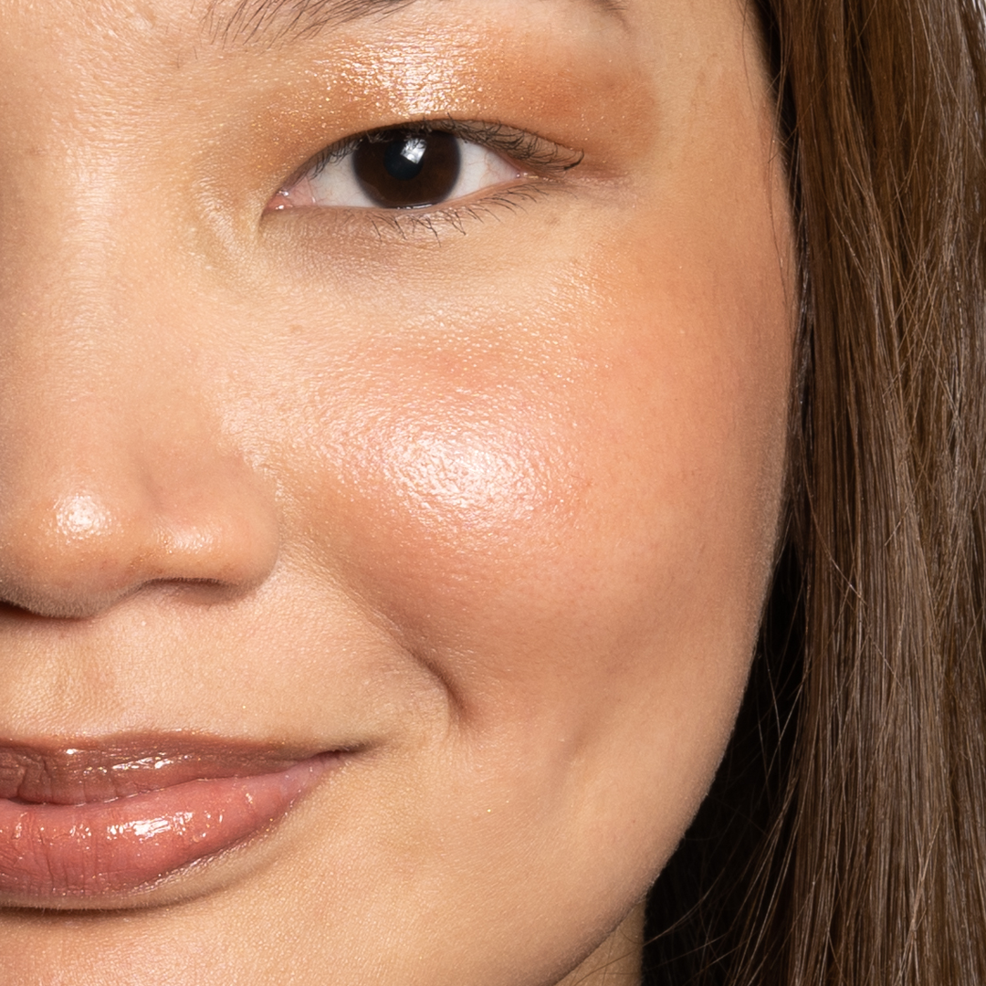 a closeup of a young woman's face, her lips, eyes and cheeks have a natural, shimmery bronze sheen to them. She is smiling.