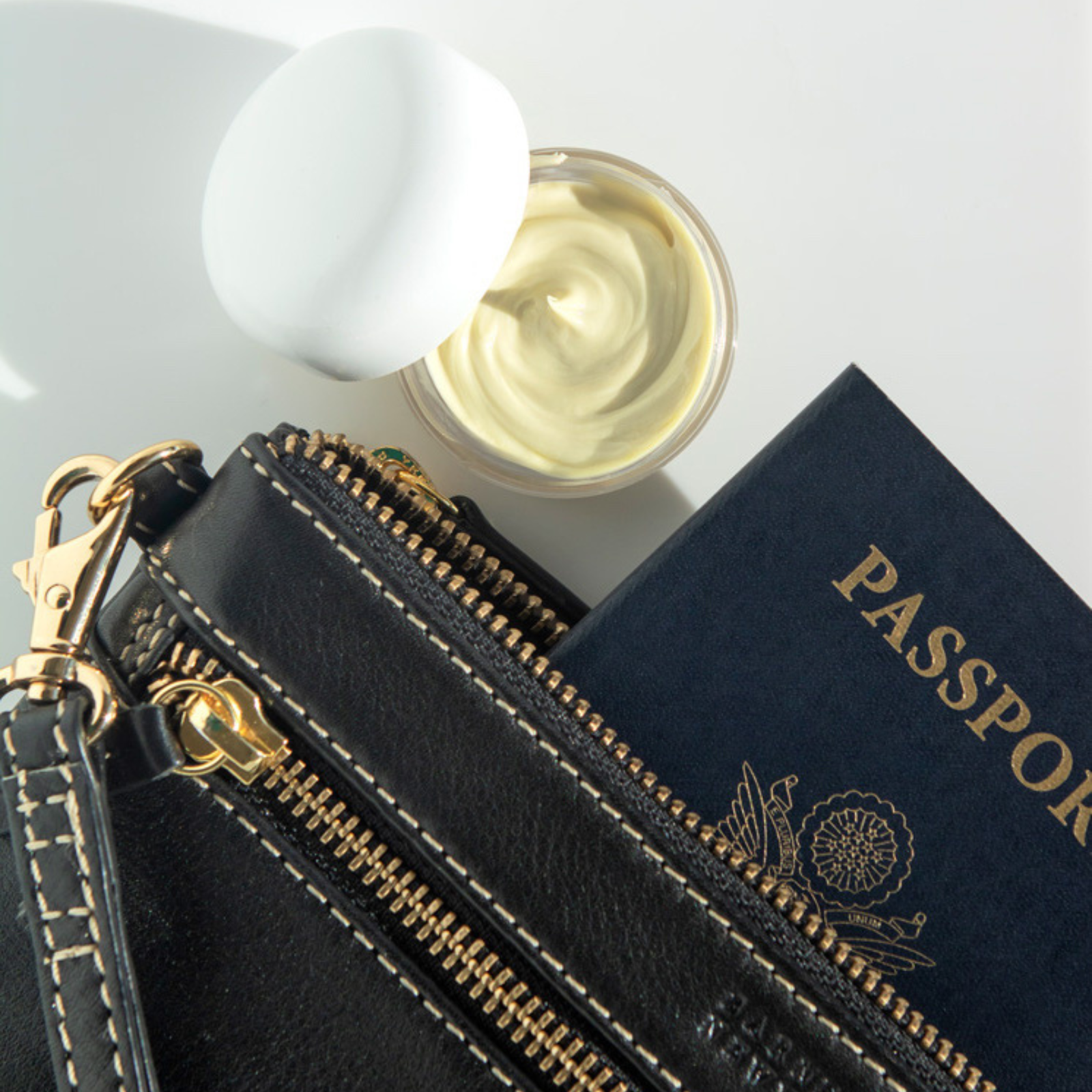 a photo of the CREAM - MINI (TRAVEL SIZE) open next to a black wallet with a passport popping out of it.