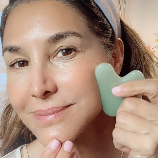 a woman holding a GUA SHA stone to her cheek and smiling.