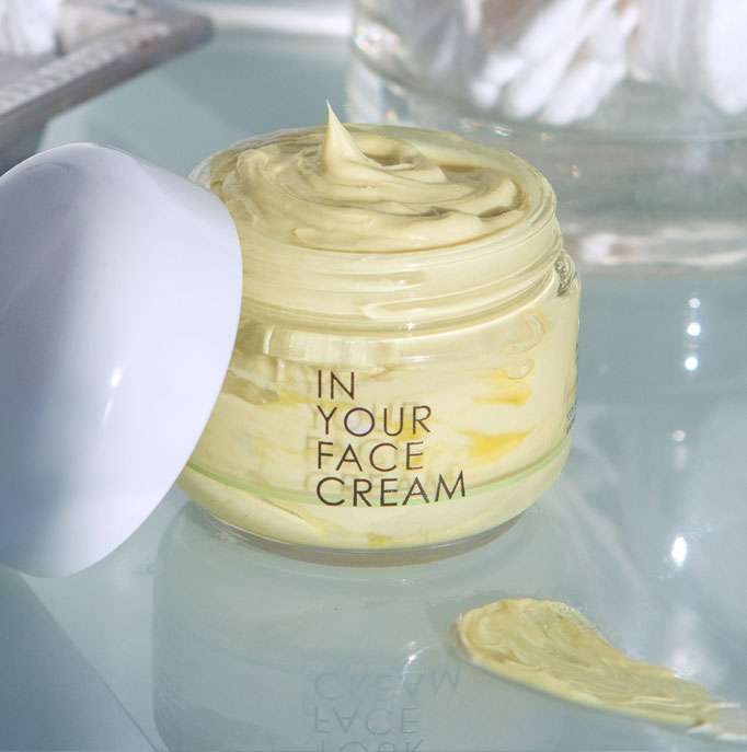 a jar of our hero product, the CREAM, with the lid open on a glass surface, showing a dollop of the cream coming out of the top