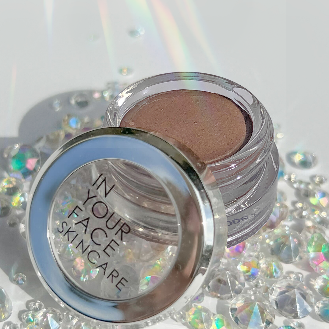 A photo of the glass jar of the SHIMMER, surrounded by sparkly little prisms that are reflecting light.