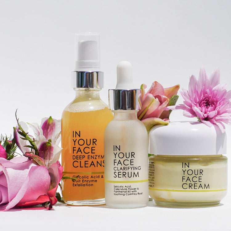 hero image with our DEEP ENZYME CLEANSE, CLARIFYING SERUM and THE CREAM, surrounded by beautiful pink flowers, on a white background