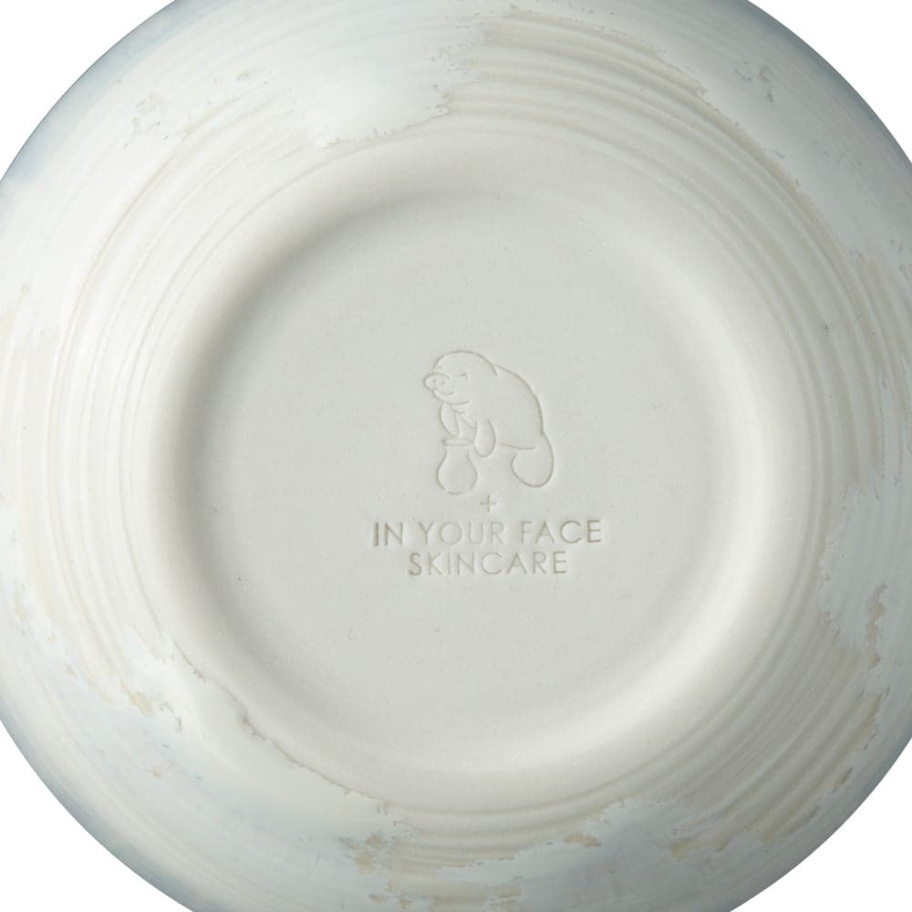 A shot of the bottom of the IN YOUR FACE BOWL, showing a stamped logo of a manatee touching a vase and a 'plus' sign and then the IN YOUR FACE SKINCARE logo below that.