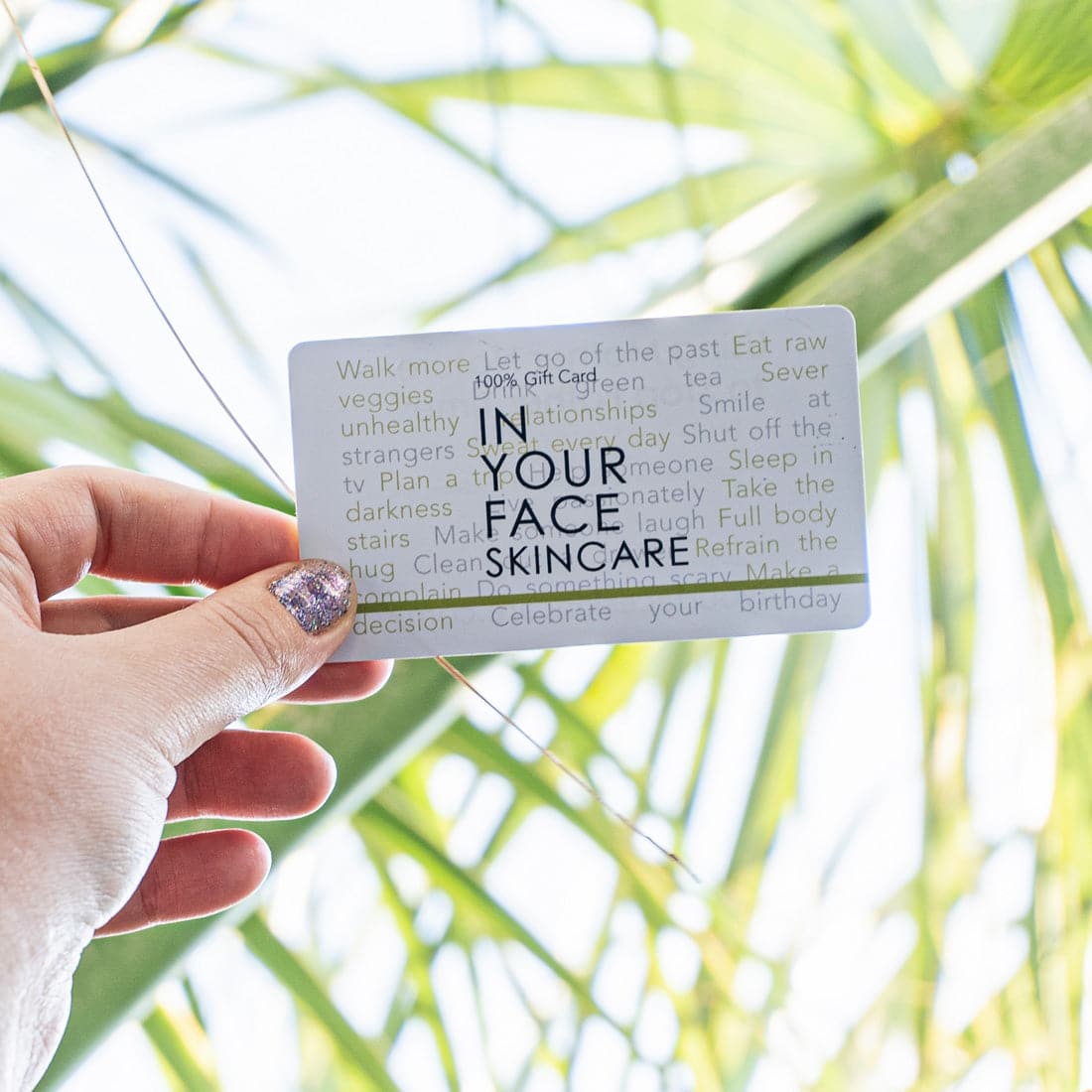 GIFT CARD held up against a bunch of palm leaves