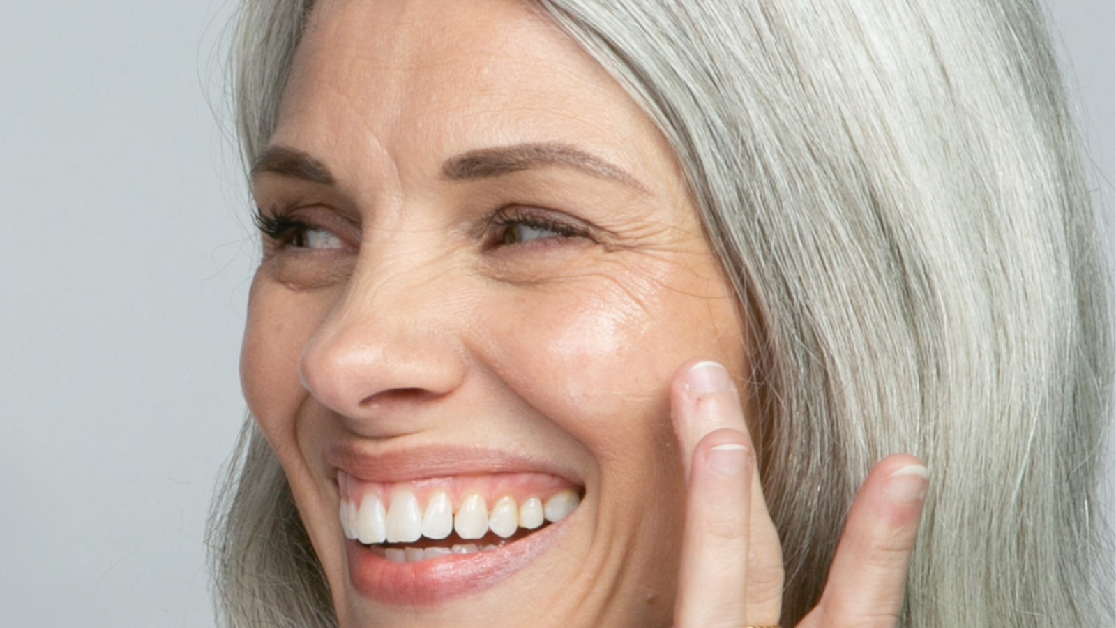 Image of woman with grey hair turneed to the side and smiling with hand up to her cheek