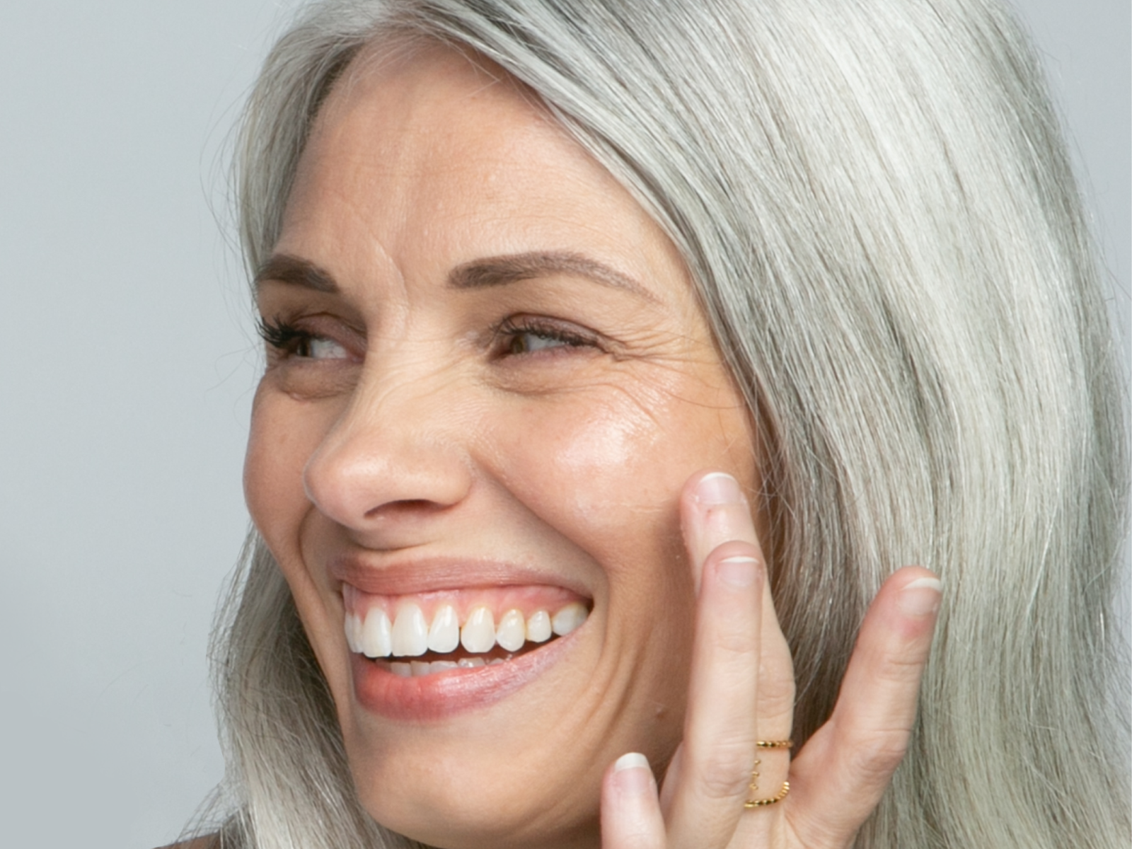 Image of woman with grey hair turneed to the side and smiling with hand up to her cheek