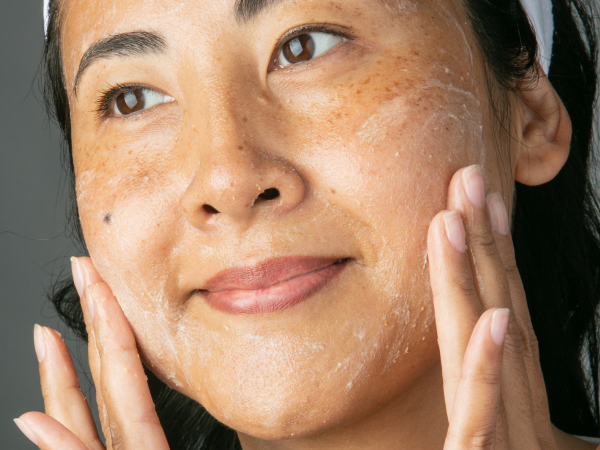 woman applying scrub to her cheeks and smiling