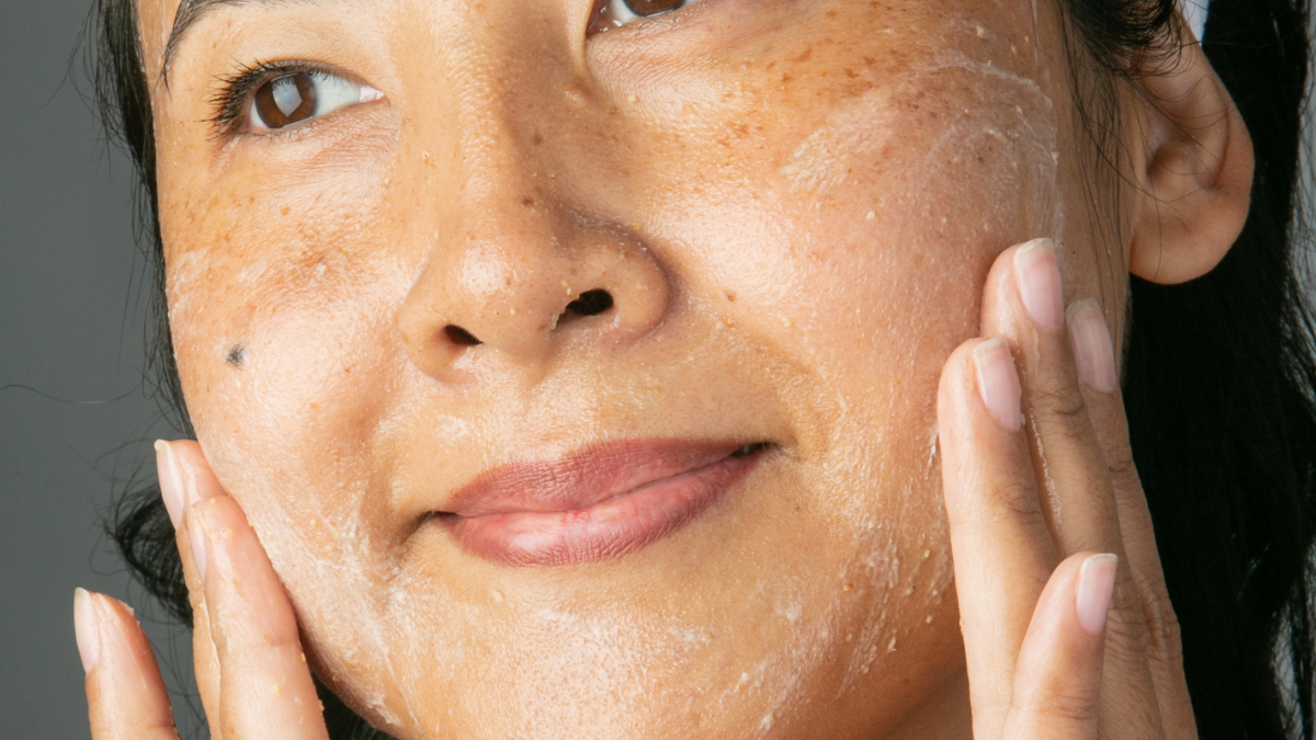 woman applying scrub to her cheeks and smiling