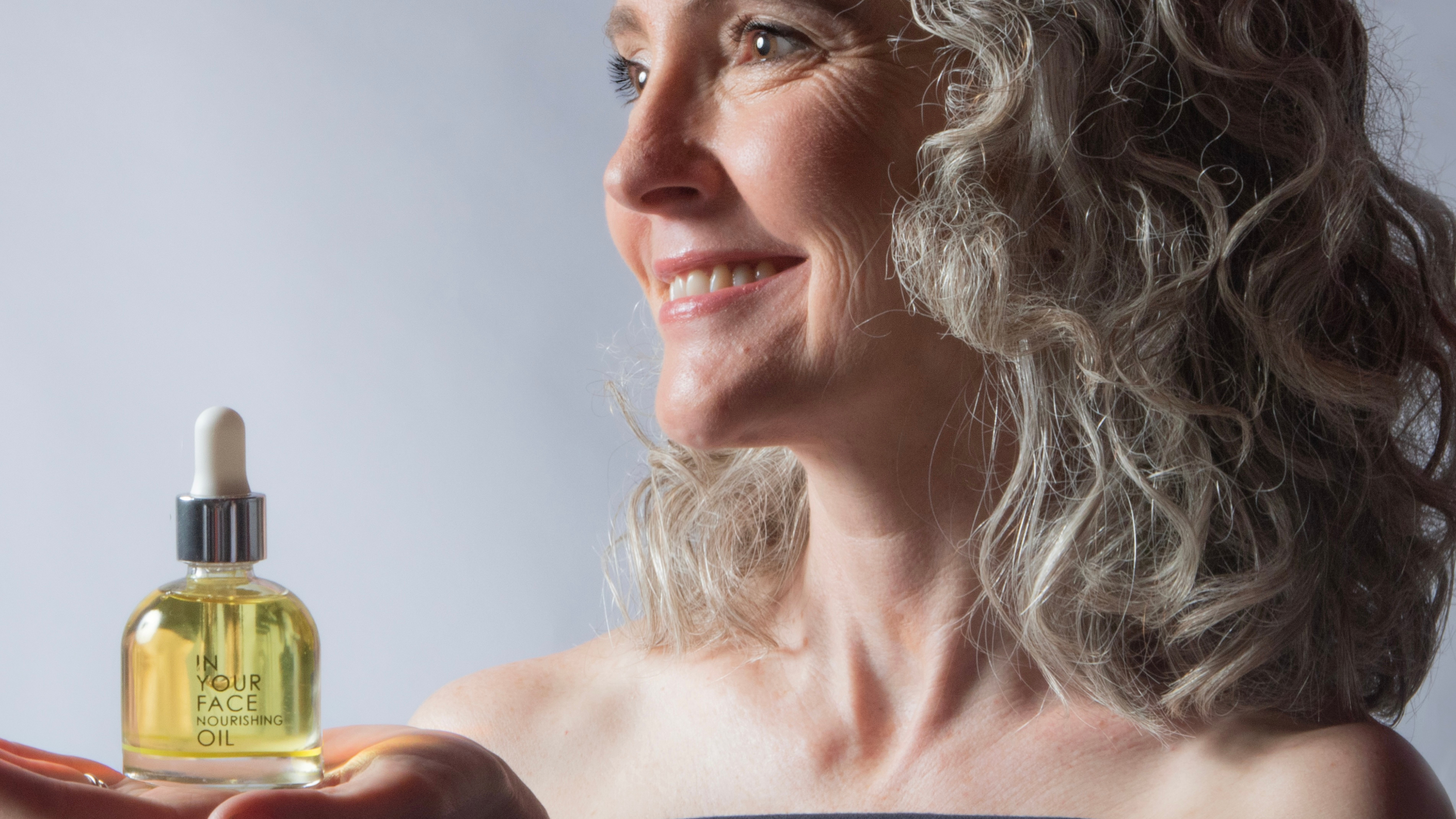 a woman with grey hair holding the NOURISHING OIL