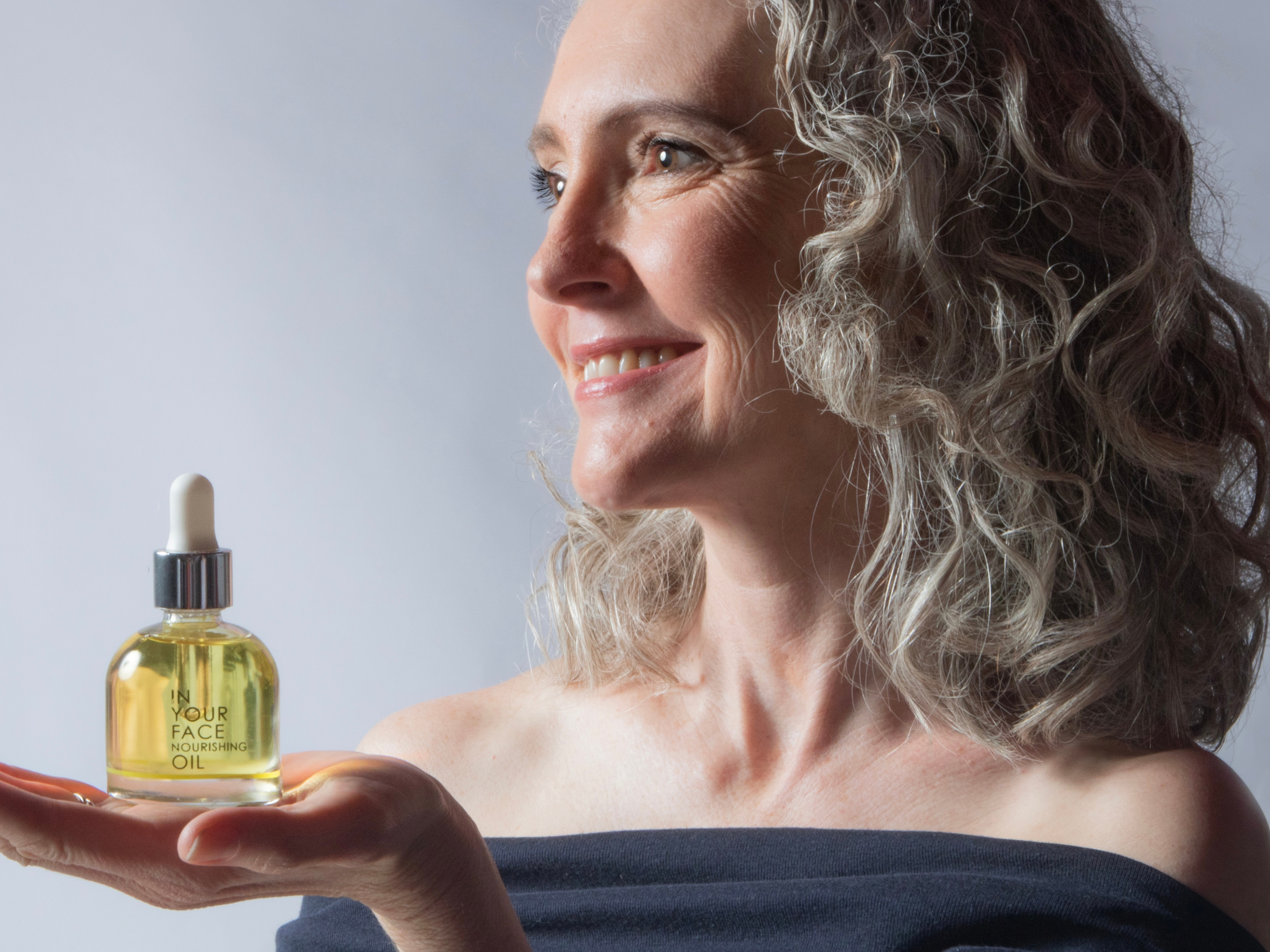 a woman with grey hair holding the NOURISHING OIL
