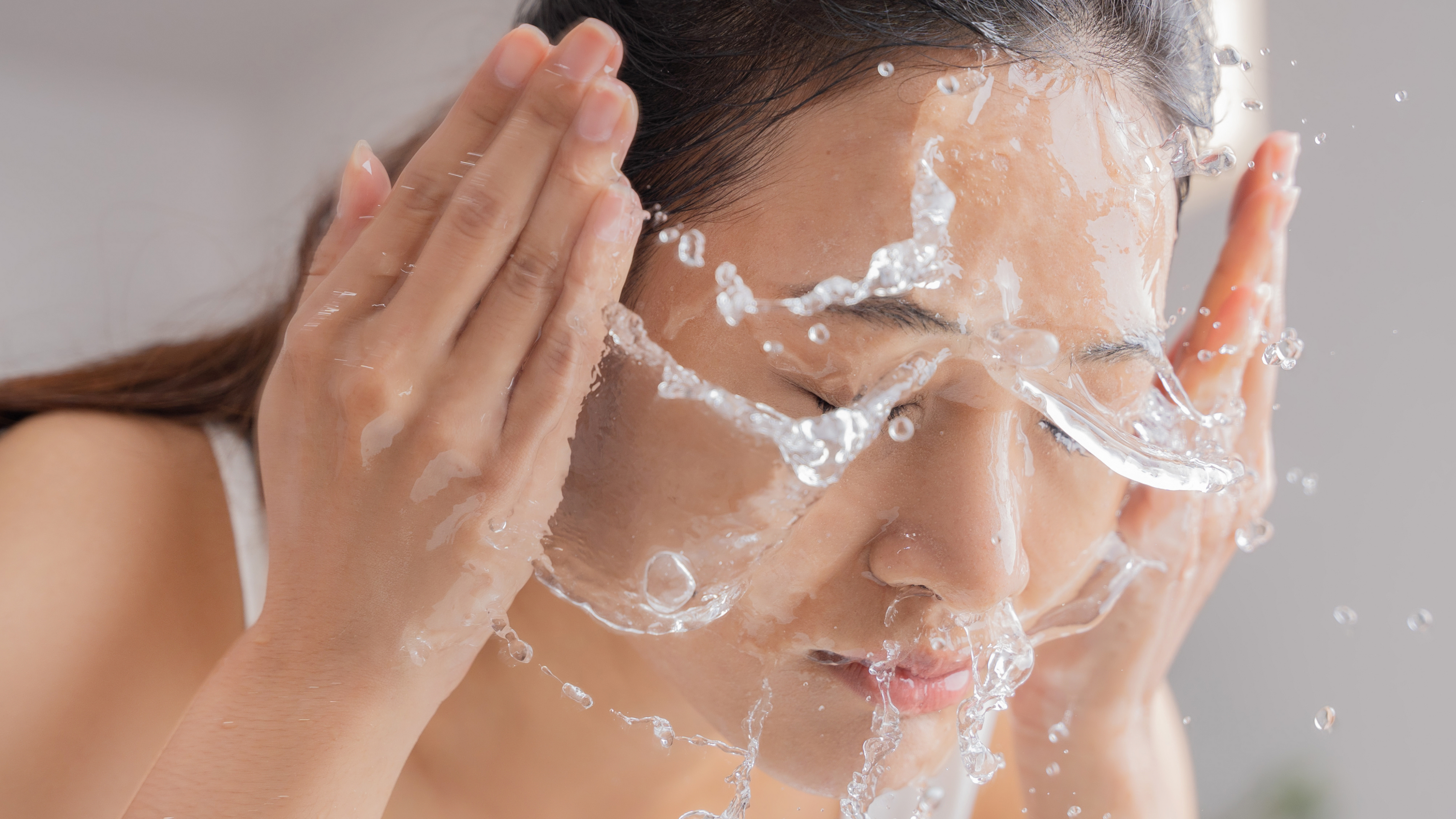 an asian woman splashing her face with water