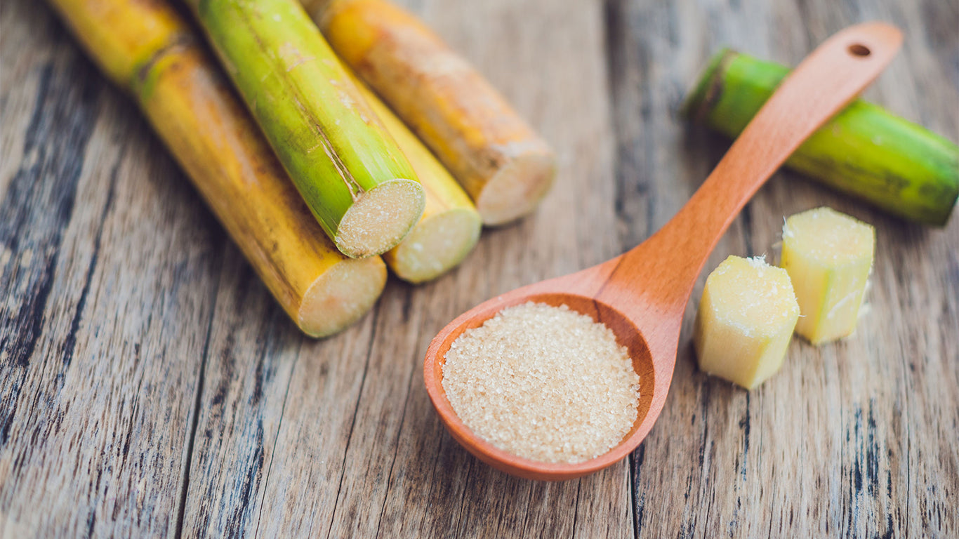 An image of sugar cane stalks and crystals in a spoon on wooden background