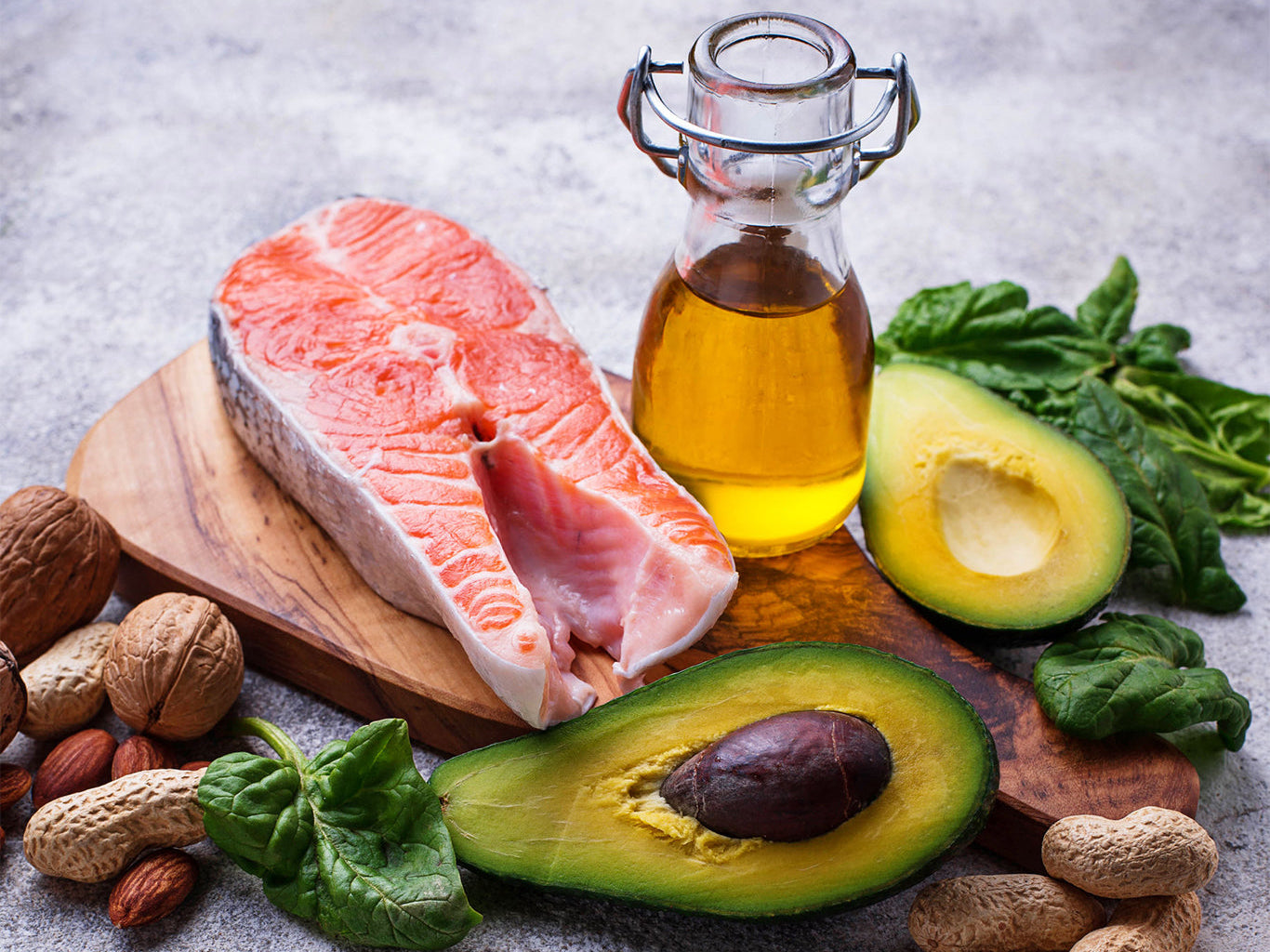 an jar of olive oil surrounded by foods with healthy fats like salmon and avocados