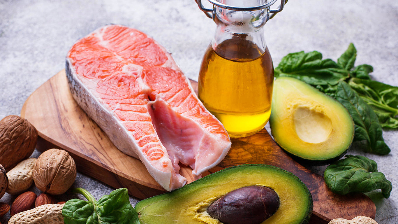 an jar of olive oil surrounded by foods with healthy fats like salmon and avocados