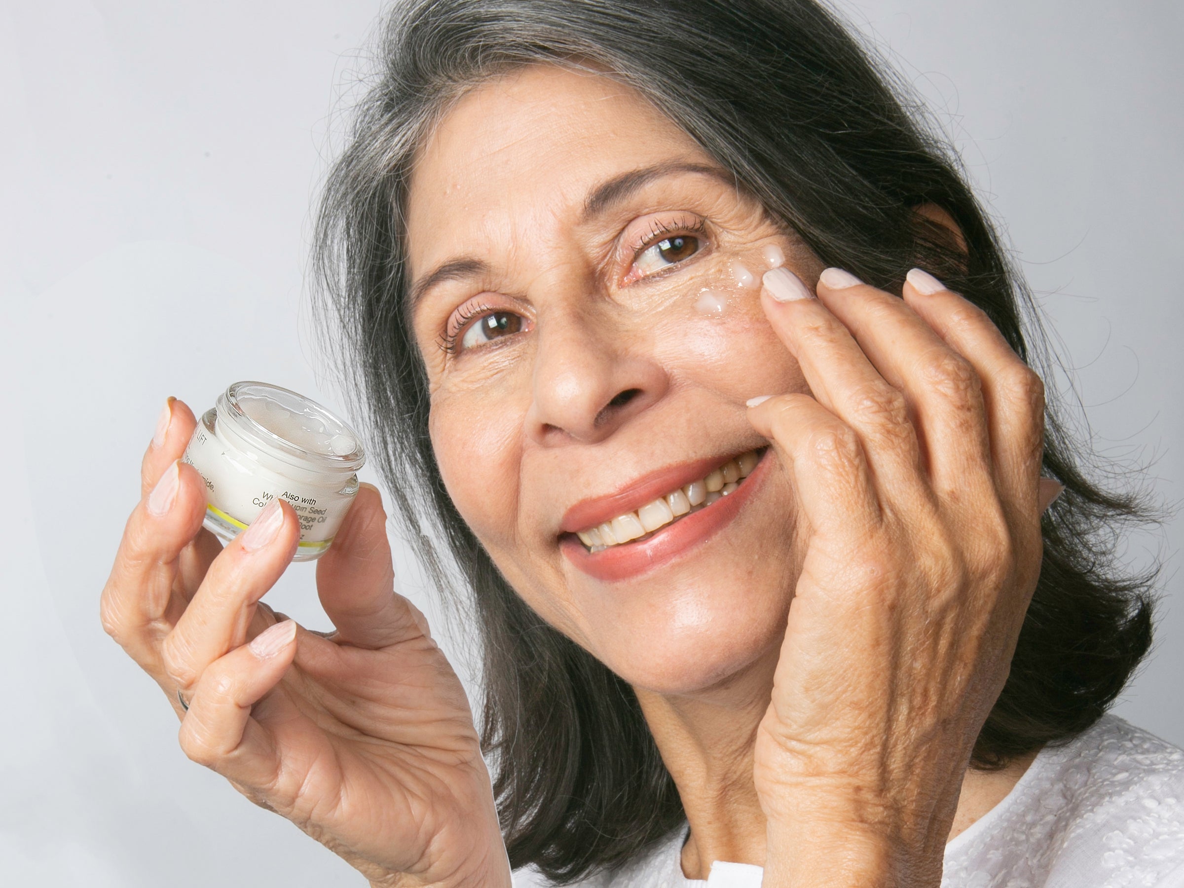 woman holding cucumber slices to her eyes on a pink background