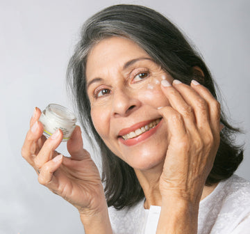 woman holding cucumber slices to her eyes on a pink background