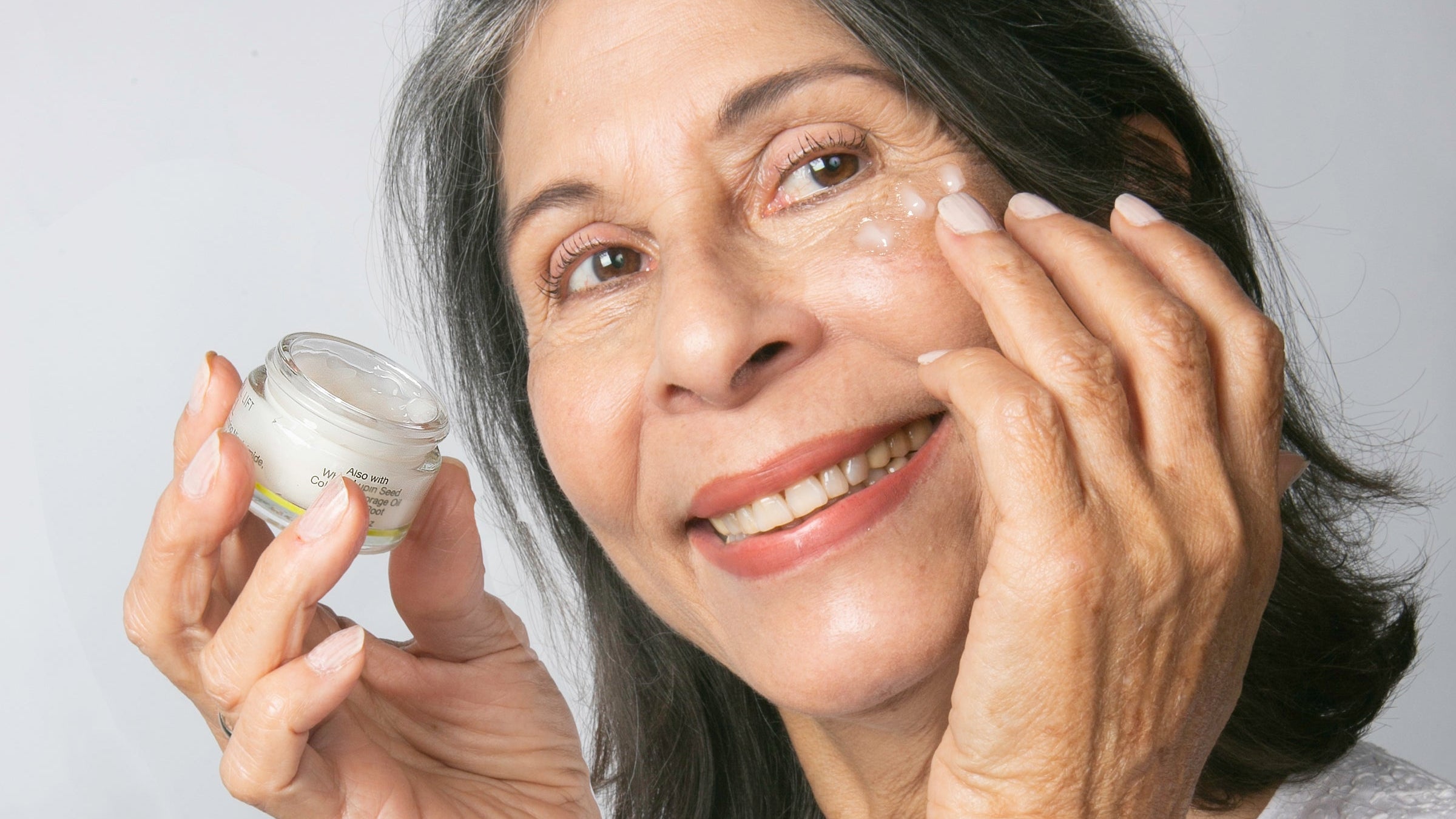 woman holding cucumber slices to her eyes on a pink background