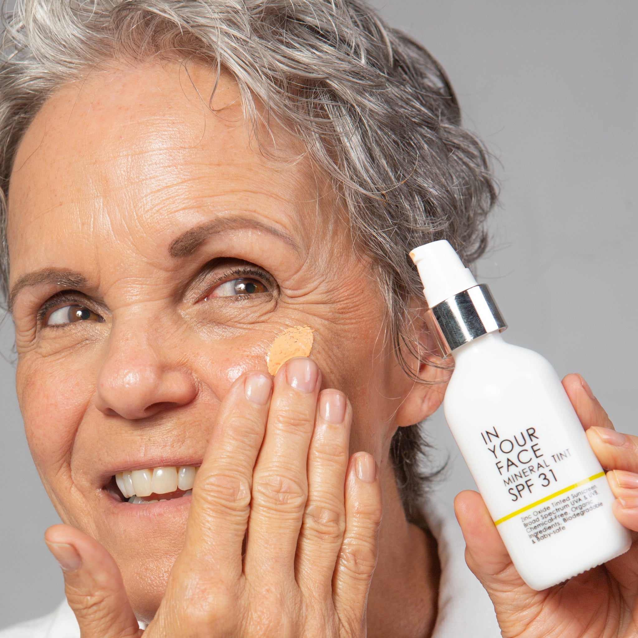 Smiling mature woman applying SPF product to cheek