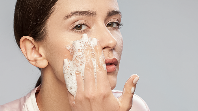 Young woman washing her face against a grey background