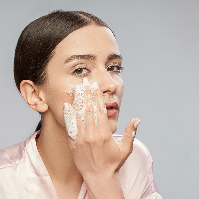 Young woman washing her face against a grey background