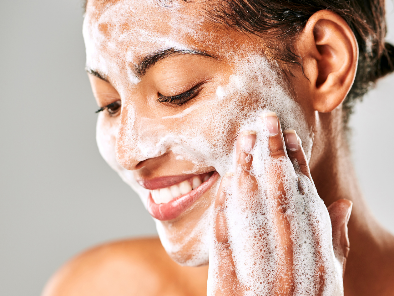 a medium-skinned woman sudsing up foam on her cheek and smiling