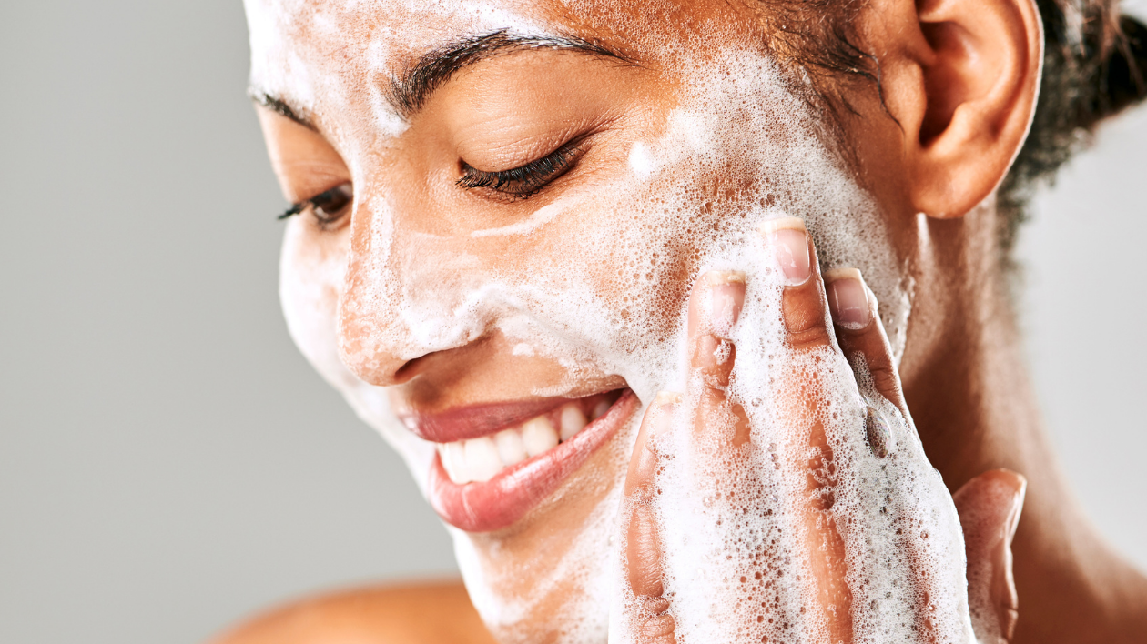 a medium-skinned woman sudsing up foam on her cheek and smiling