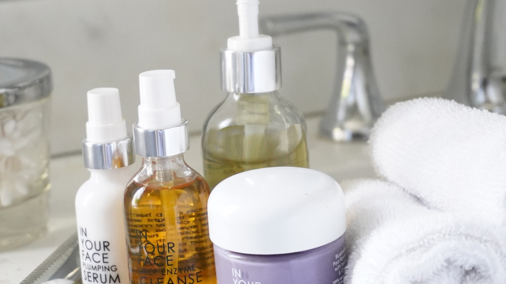 Easy Steps to a Basic Skincare Routine! A group of IN YOUR FACE SKINCARE products on a tray in a bathroom with a faucet behind them and towels beside them