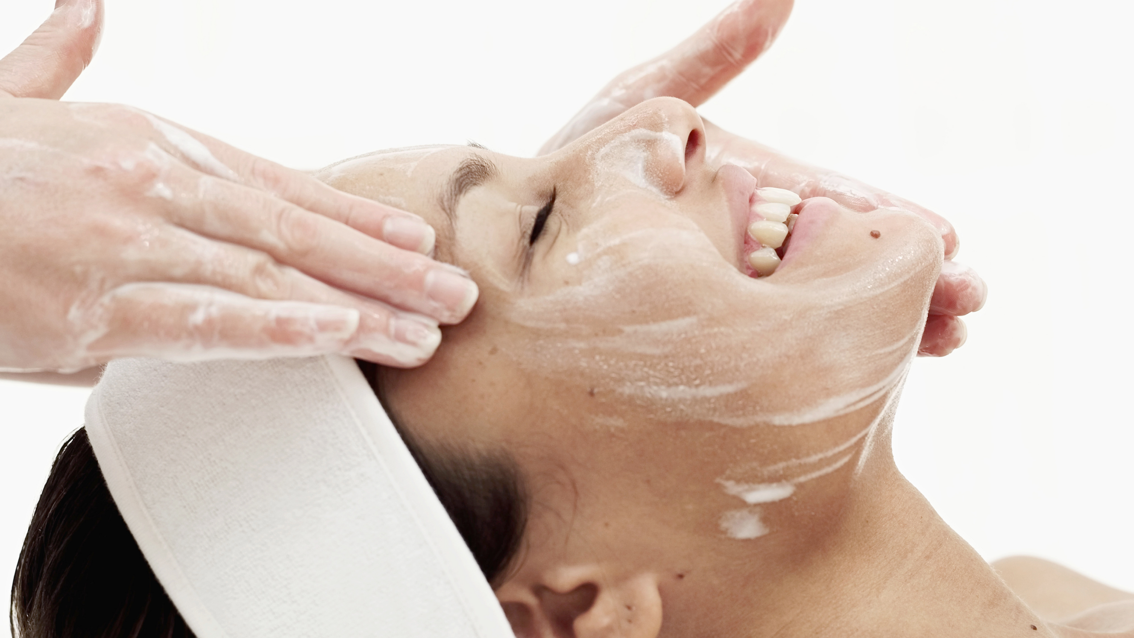 a woman smiling, getting a facial on a white background
