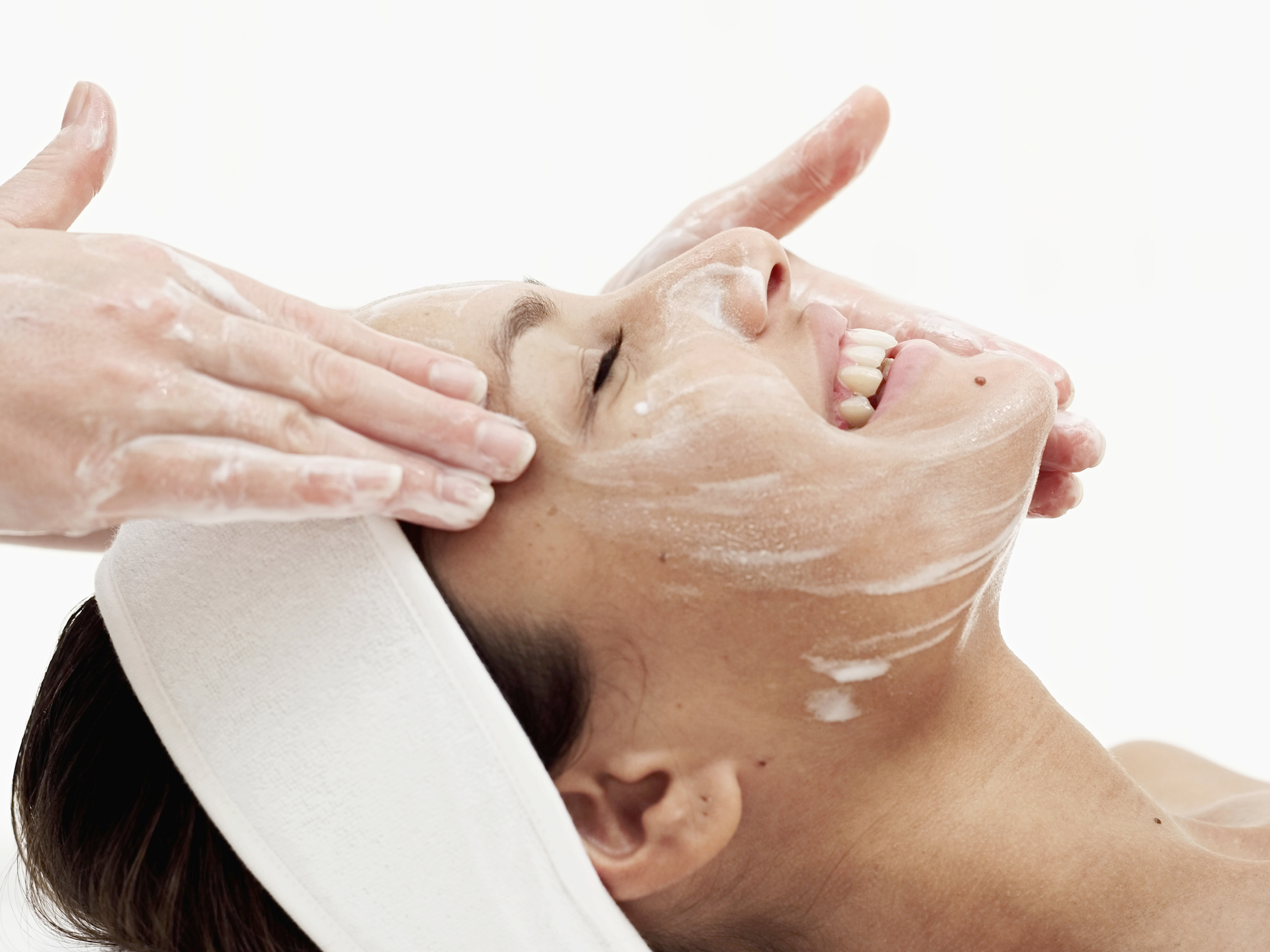 a woman smiling, getting a facial on a white background