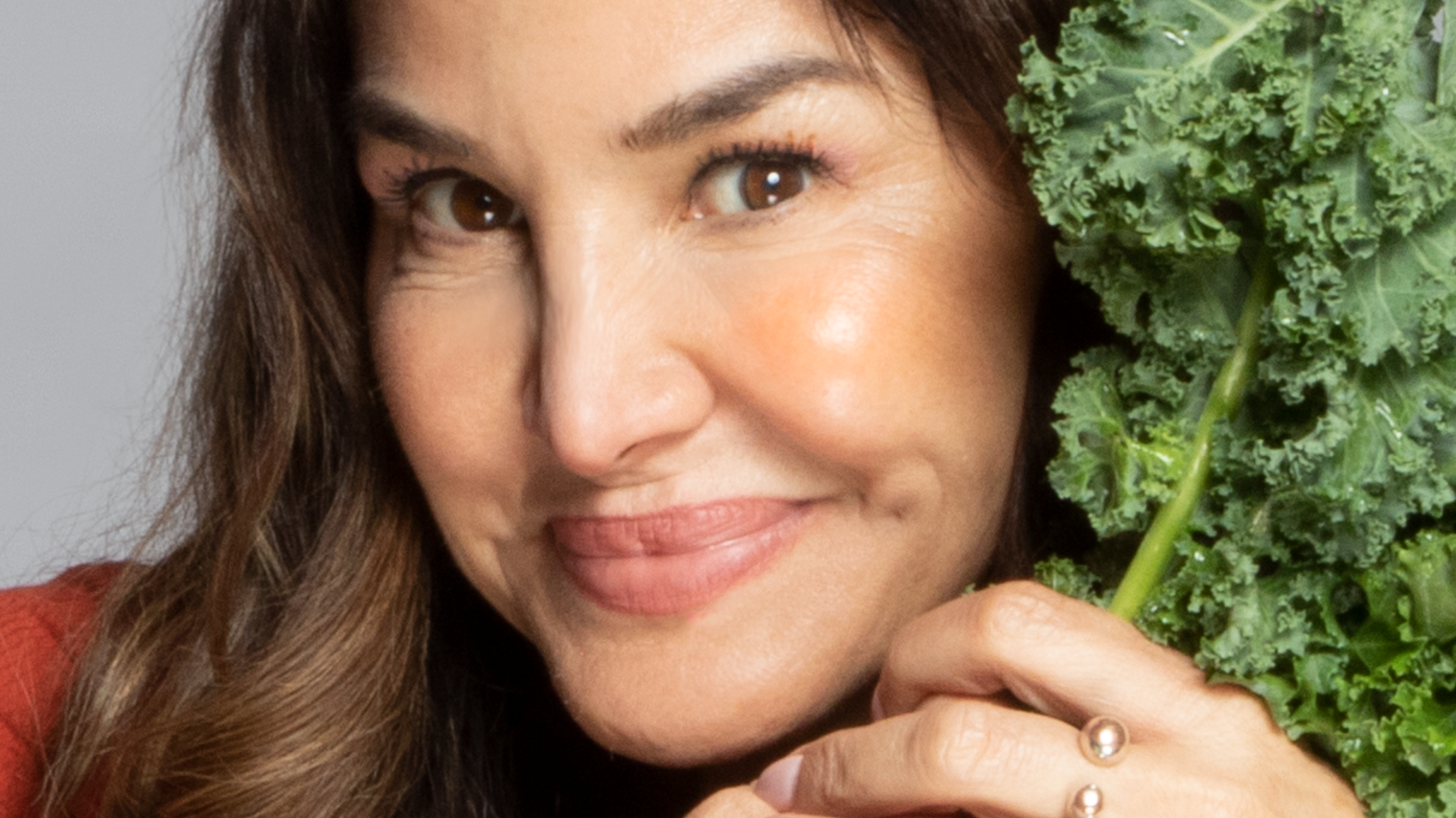 a woman holding kale next to her face, smiling