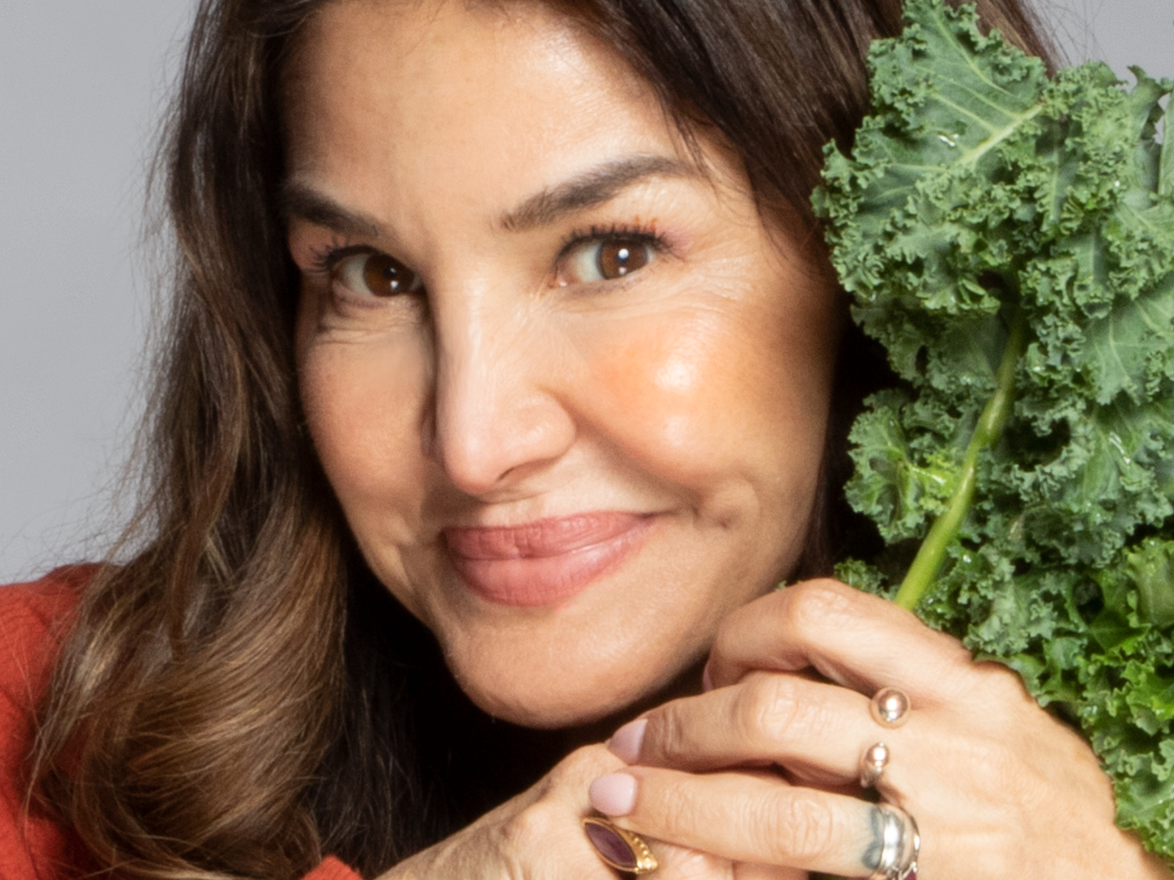 a woman holding kale next to her face, smiling