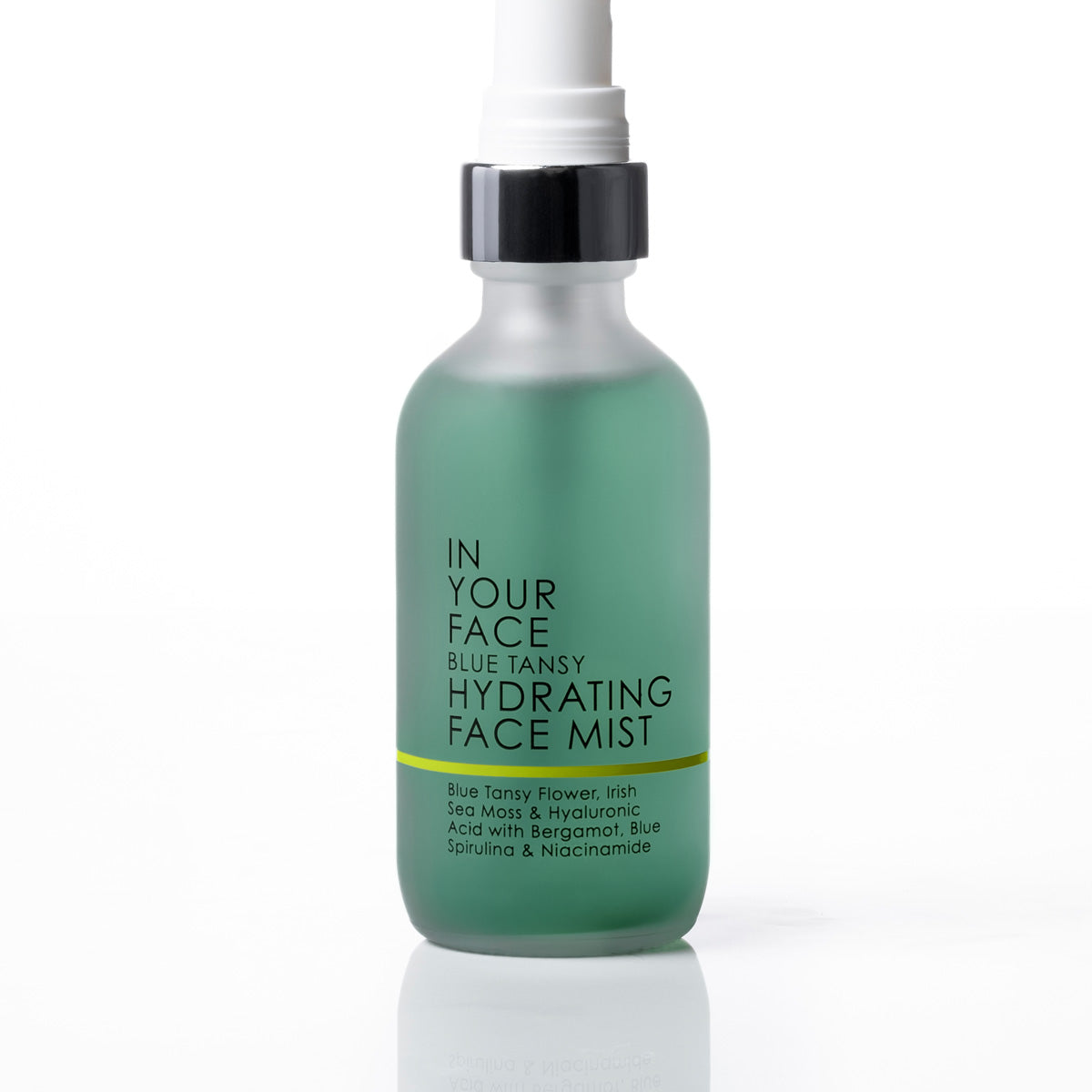 A frosted glass spray bottle of IN YOUR FACE Blue Tansy Hydrating Face Mist, filled with a translucent mint green liquid, featuring a black collar and white spray nozzle, set against a clean white background.