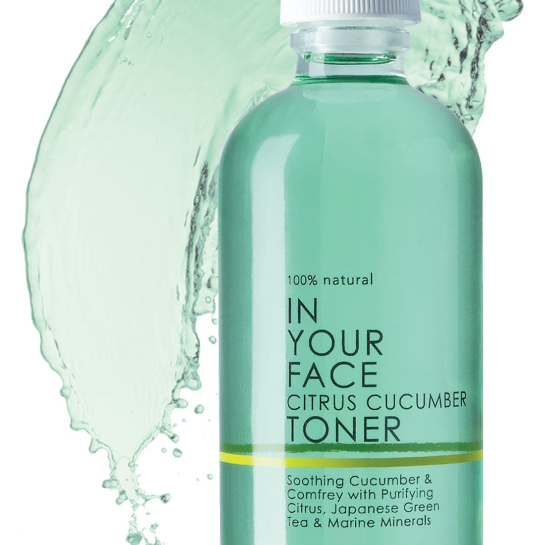 A bottle saying "100% Natural IN YOUR FACE CITRUS CUCUMBER TONER" on a white background. It is a pretty light aqua and in a clear bottle. The bottle also says "Soothing Cucumber & Comfrey with Purifying Citrus, Japanese Green Tea & Marine Minerals", showing a splash of the liquid toner in the background.