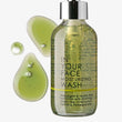 Bottle of 'In Your Face' moisturizing wash with green liquid and droplets on a white background