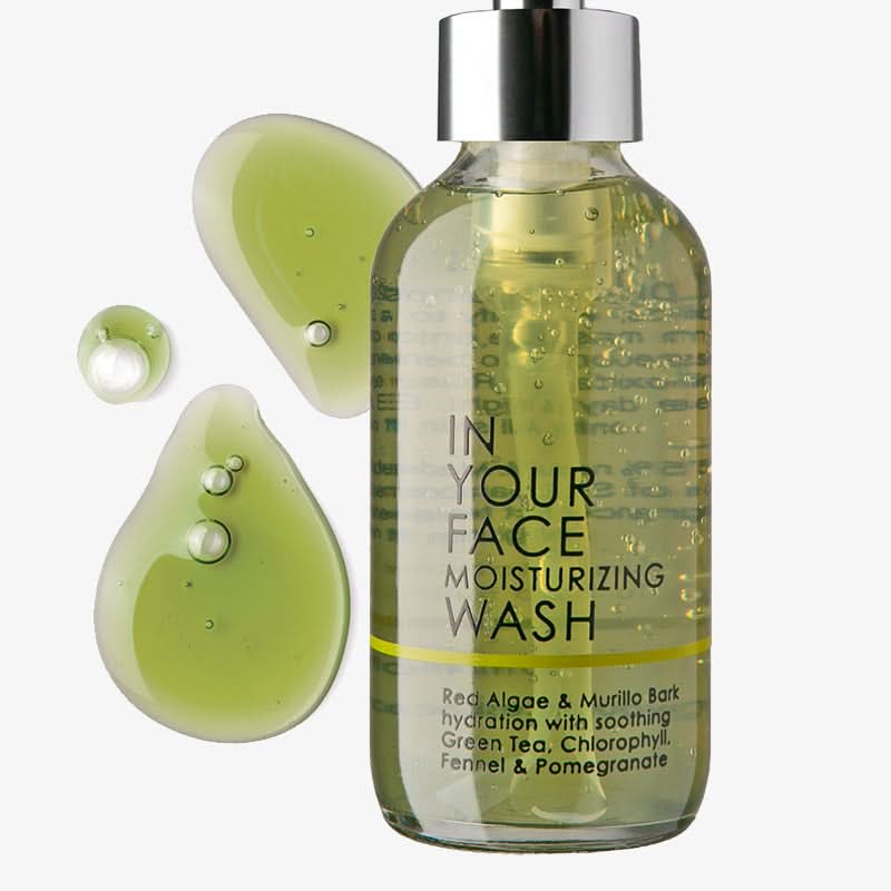 Bottle of 'In Your Face' moisturizing wash with green liquid and droplets on a white background