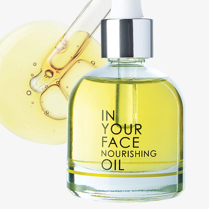 Glass bottle of 'In Your Face Nourishing Oil' with dropper on a white background