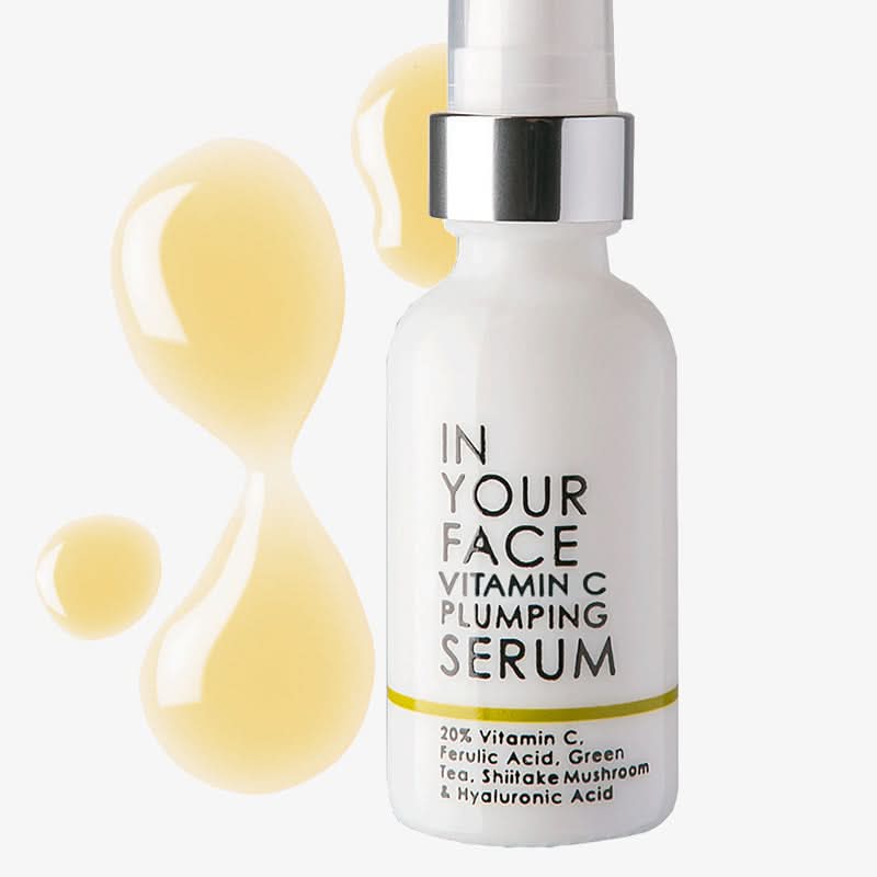 Vitamin C plumping serum bottle with yellow liquid droplets on a white background
